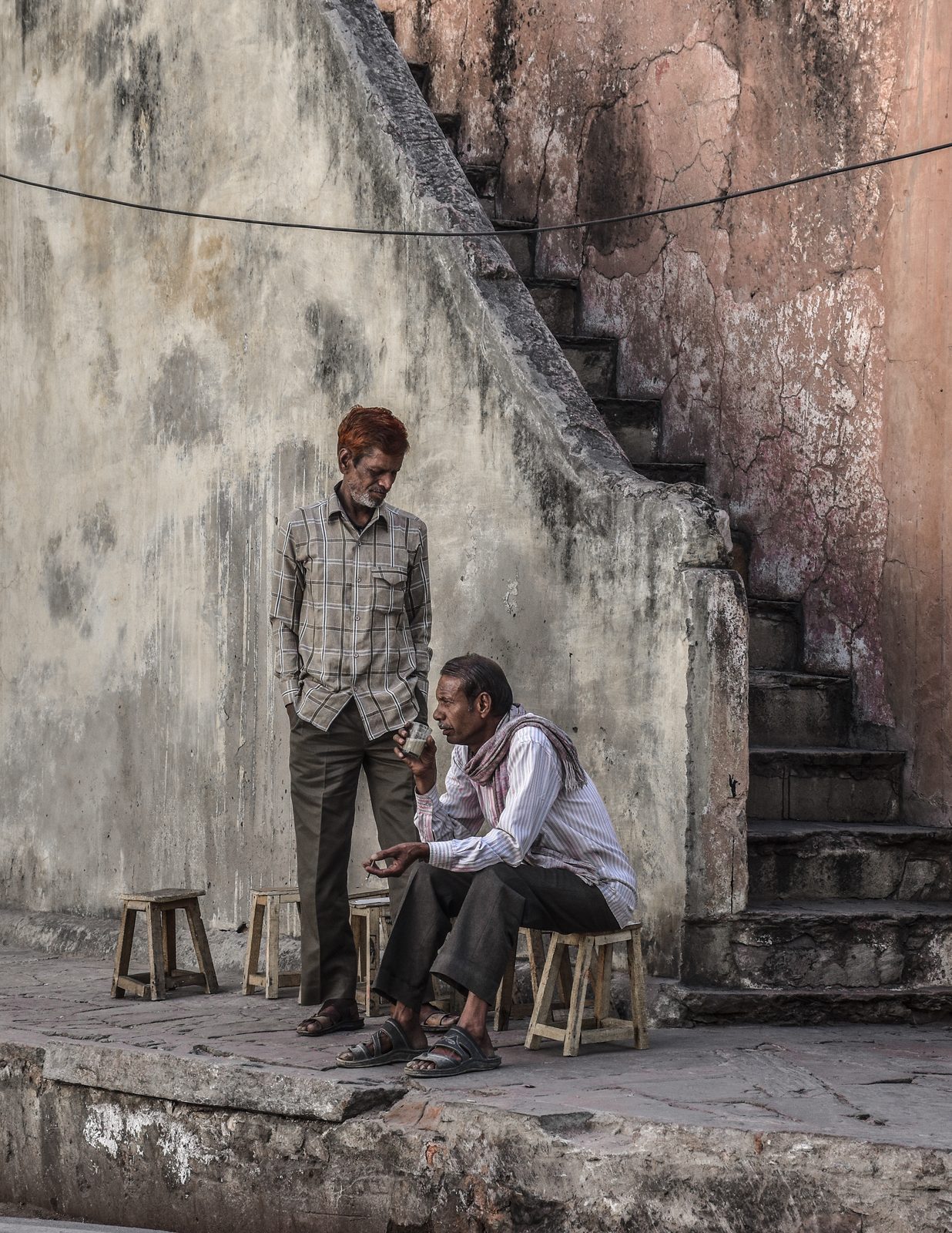 Two men with tea beside a worn staircase, Jaipur