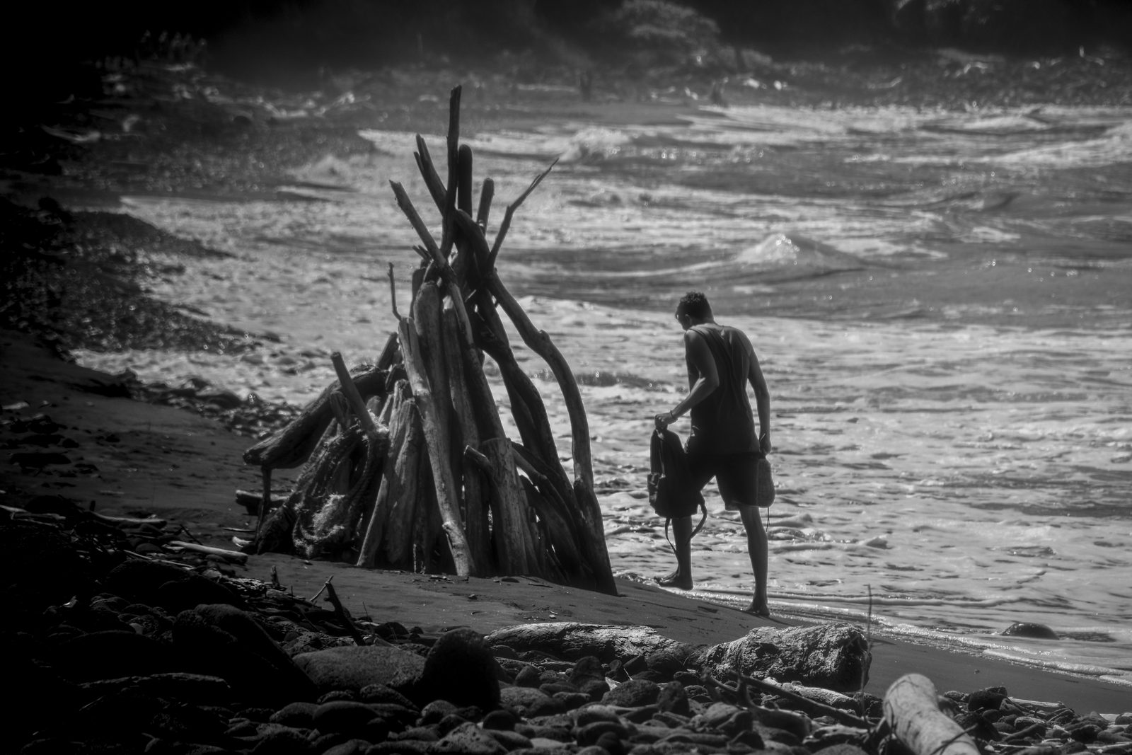 A man beside a driftwood pile on the black sand beach at Waipio Valley, Hawaii