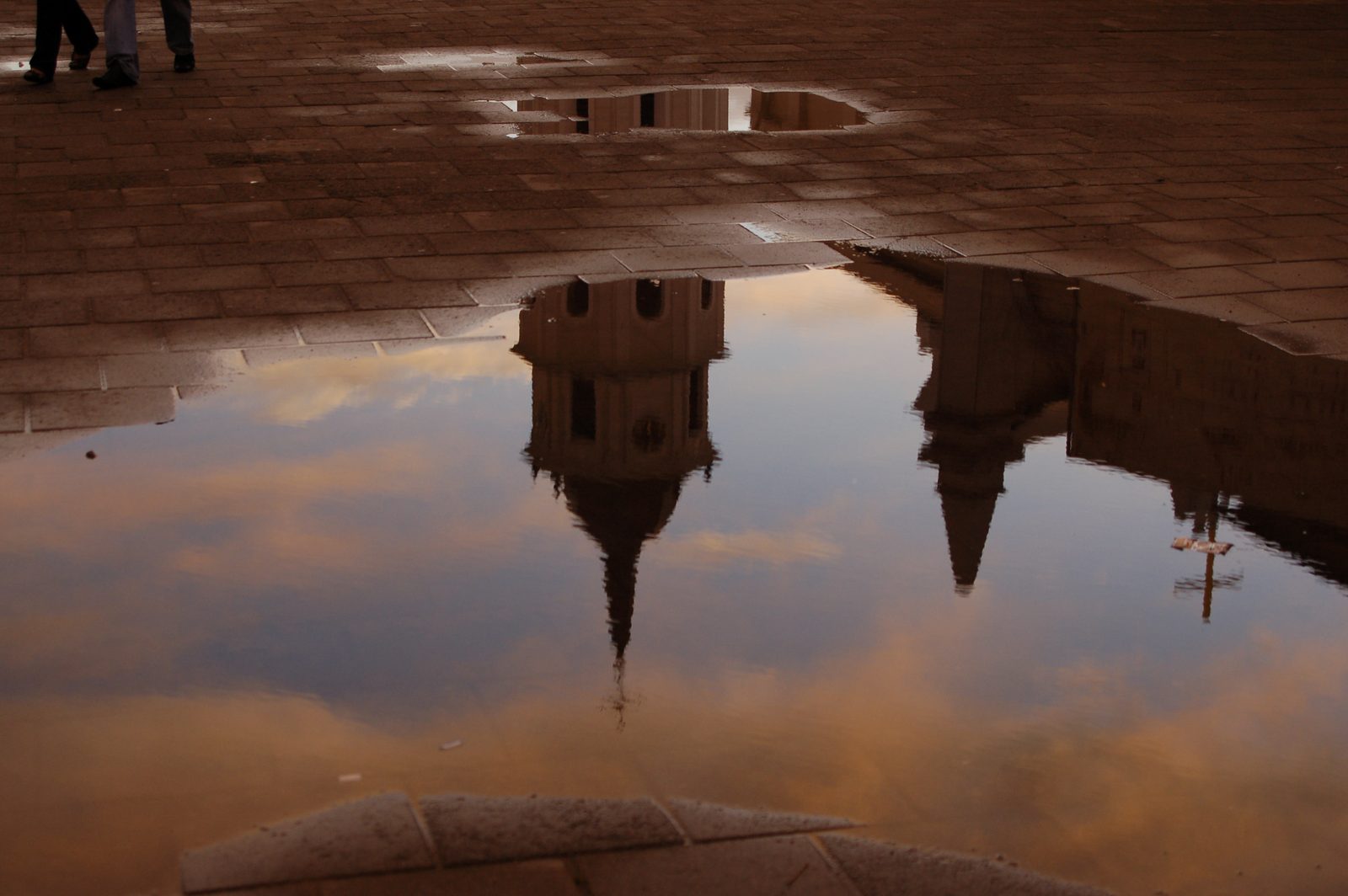 Church towers reflected in a puddle on a cobbled square, Vilnius